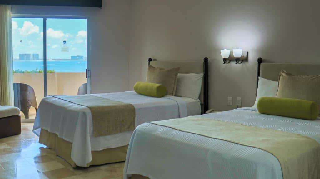 Quarto no Hotel Casa Maya com uma cama de solteiro e uma de casal, uma varanda, tudo decorado em bege e verde, para hotéis em Cancun