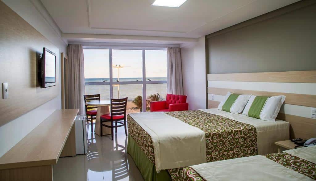 Quarto no Laguna Praia Hotel com piscina de casal, com uma mesa de dois lugares, uma poltrona e uma sacada com vista para o mar, uma televisão e um frigobar, para representar resorts em João Pessoa
