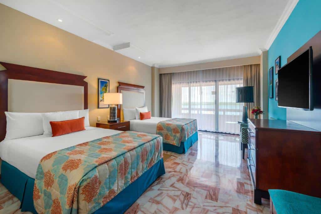 Quarto no Omni Cancun Hotel & Villas All Inclusive com uma cama de casal, uma de solteiro, uma sacada ampla, uma televisão, tudo decorado em azul, branco e laranja