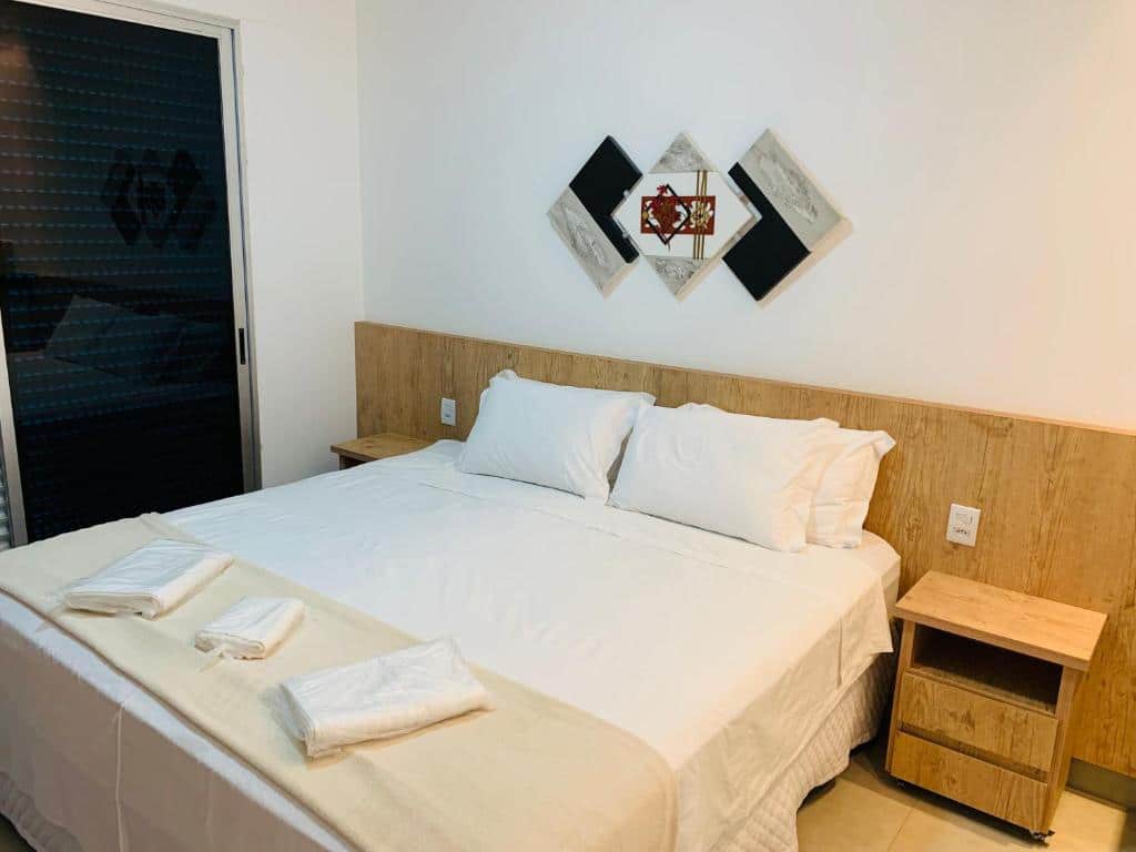 Quarto na Pousada do Batata, uma cama de casal, uma sacada, um quadro e duas mesinhas de cabeceira, toalhas e travesseiros estão sob a cama, para representar pousadas em Escarpas do Lago