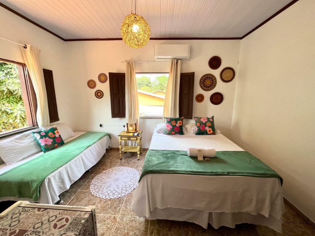 Quarto na Pousada Ocazum, uma cama de casal, uma janela, um ar-condicionado, um sofá-cama, tudo decorado de forma rústica e em tons de verde, branco e marrom