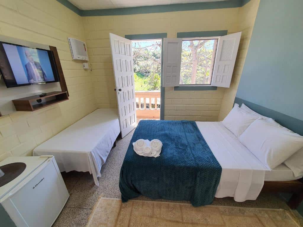 Quarto da Pousada ponta de areia com uma cama de casal, uma de solteiro, um frigobar, uma televisão e uma janela, para representar pousadas em Vila Velha