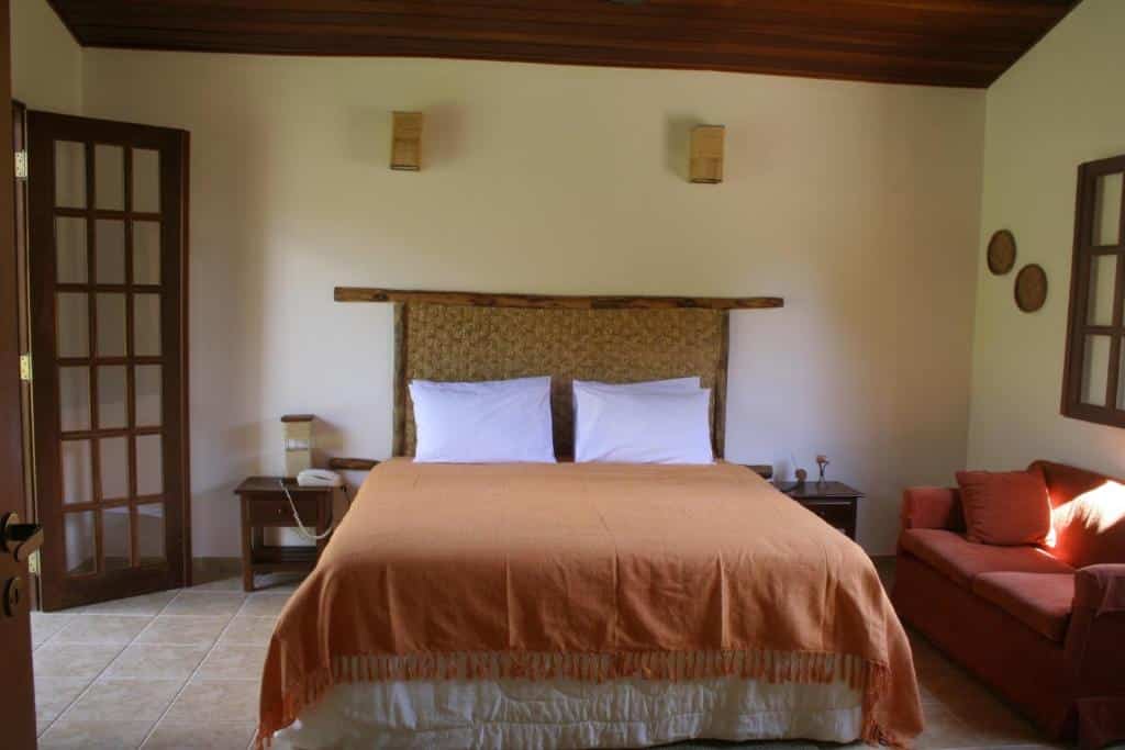 Quarto na Pousada Vale das Araras com uma cama de casal, alguns detalhes rústicos na decoração, um pequeno sofá e uma varanda