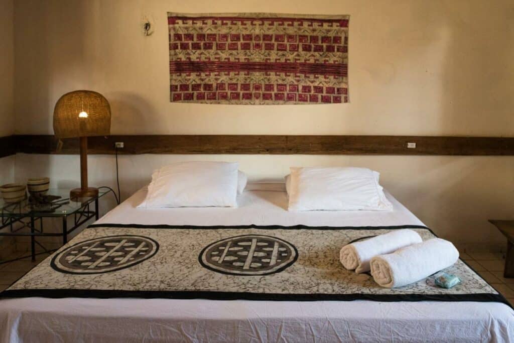 Quarto no Quintal da Cuiarana, local amplo, com travesseiros e toalhas sob a cama, com detalhes rústicos, para representar pousadas em Alter do Chão