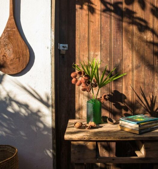 Detalhes na entrada do Quintal da Cuiarana, tudo em madeira, uma mesa com livros e um vaso de flores