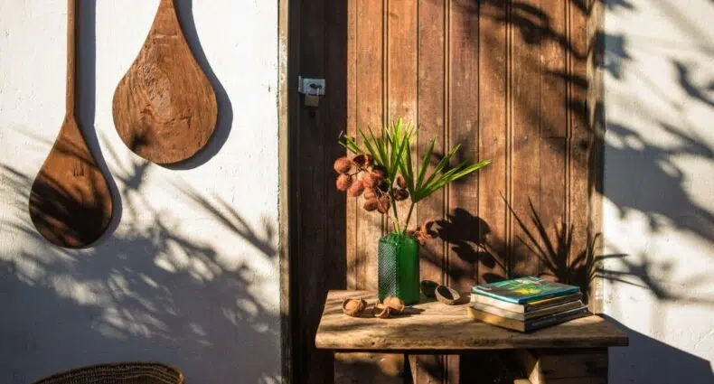 Detalhes na entrada do Quintal da Cuiarana, tudo em madeira, uma mesa com livros e um vaso de flores