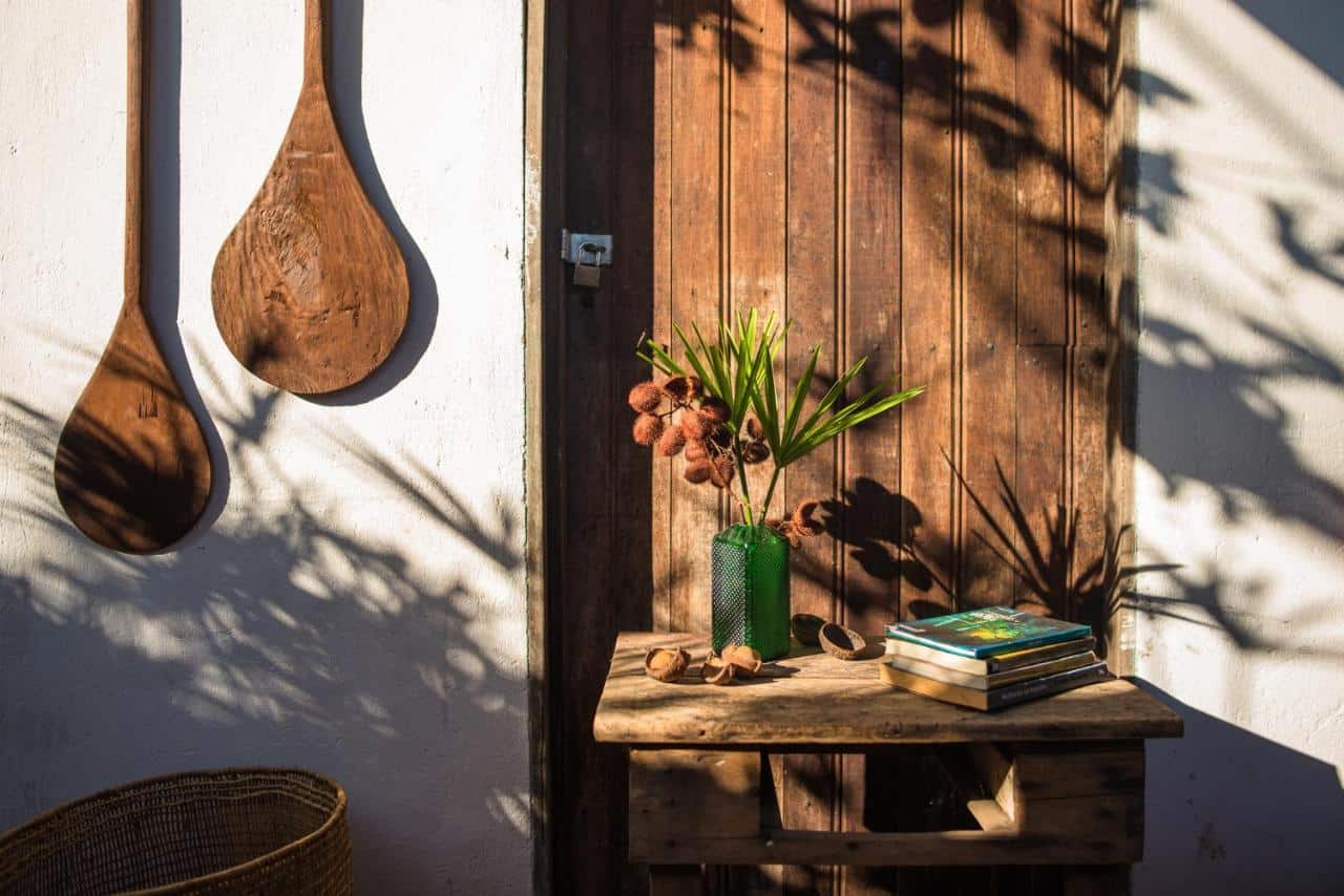 Detalhes na entrada do Quintal da Cuiarana, tudo em madeira, uma mesa com livros e um vaso de flores