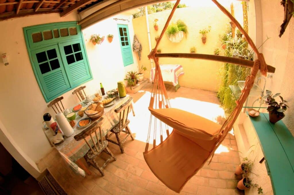 Quintal na Pousada Flor de Olinda com uma mesa com cadeiras de madeira e algumas redes