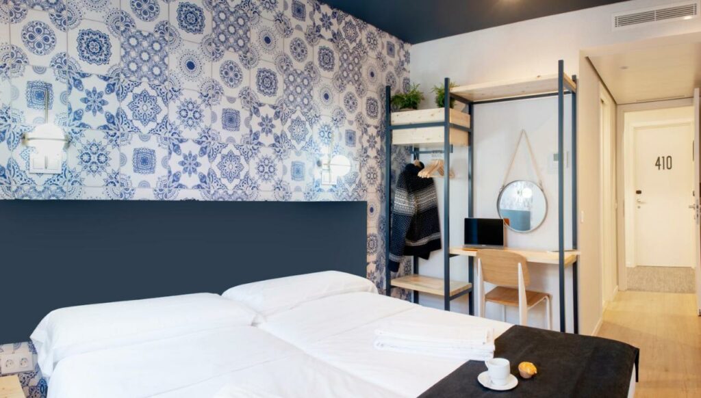 Quarto no hostel Rodamon Lisboa, uma das alternativas aos hotéis em Lisboa, com duas camas de solteiro juntas, formando uma cama de casal, uma penteadeira com espelho e notebook, e um armário aberto