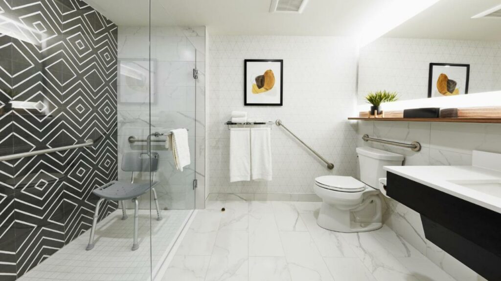 Banheiro no Stay Inn Hotel Toronto com adaptações para pessoas com deficiência, barras de apoio, pia mais baixa, cadeira dentro do boa, ambiente espaço e de fácil locomoção, para representar hotéis em Toronto