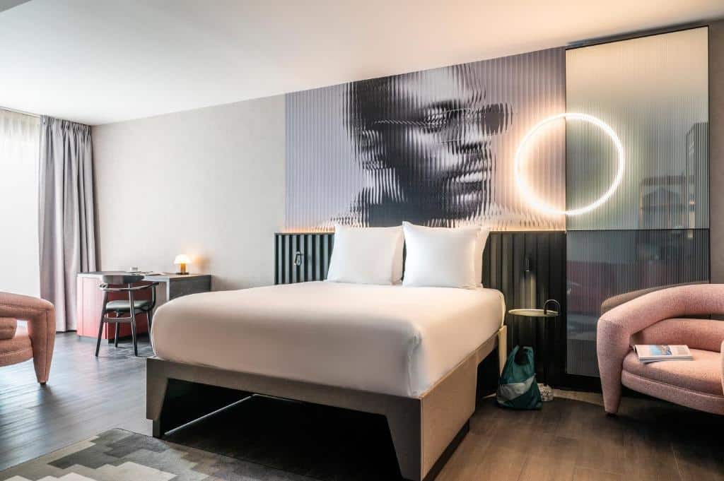 Quarto do Tribe Amsterdam, de 32 m², com cama de casal, uma poltrona e uma mesinha com cadeira. Em cima da cama, há um quadro com o rosto de de um rapaz negro de óculos escuro