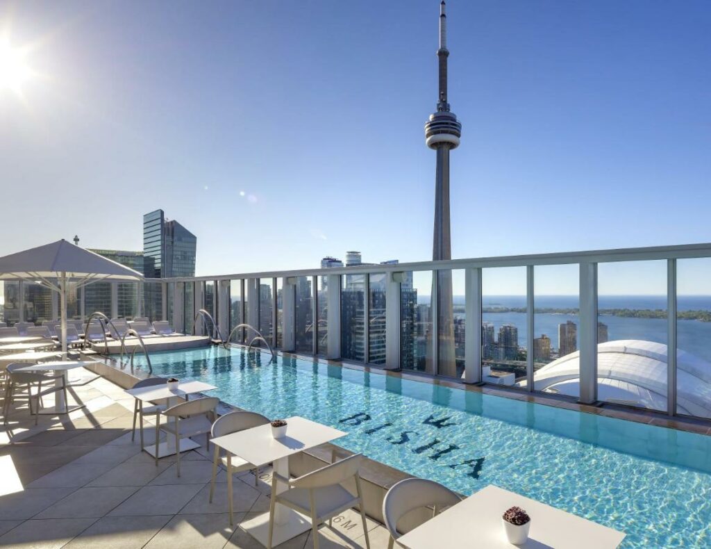 Terraço do Bisha Hotel Toronto com uma pequena piscina dando vista para o centro de Toronto com um deck cercado por mesas e cadeiras