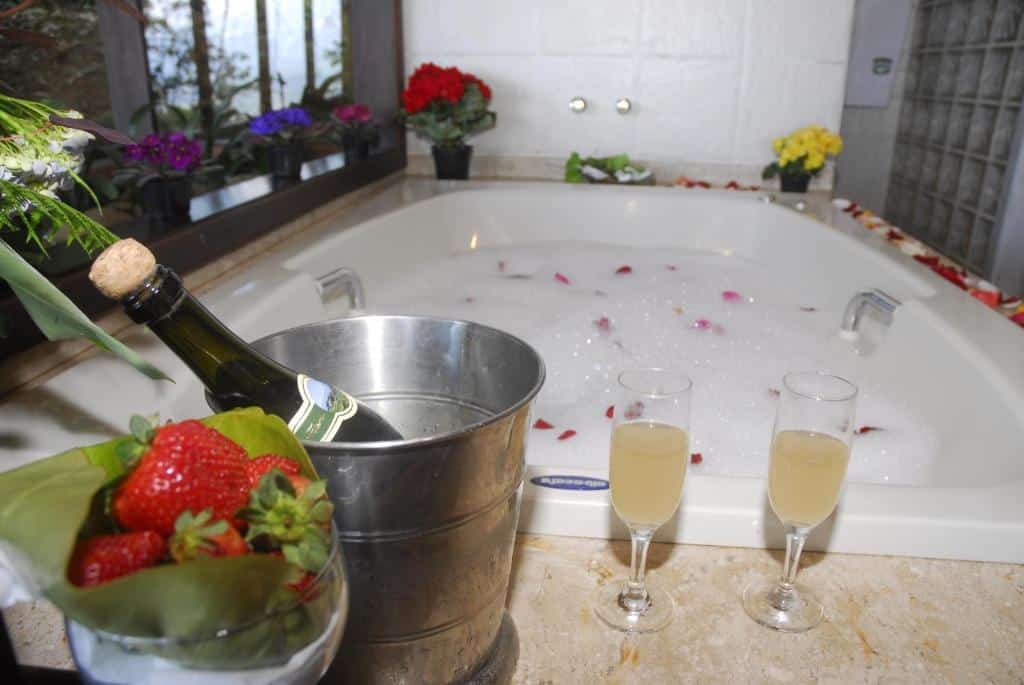 Banheira no Vista Linda Hotel com pétalas de rosas dentro e ao redor, uma garrafa de champanhe e taças
