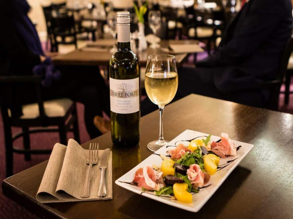 Vista de uma mesa do Academy Plaza Hotel com uma prato colorido, uma taça e uma garrafa de vinho ao lado