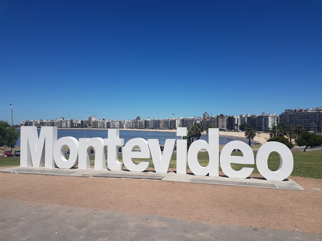 Placa escrito Montevideo com a praia e os prédios ao fundo