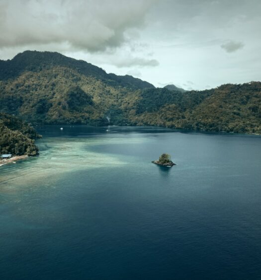 Um mar com azul bem escuro levando em direção de uma ilha com uma pequena embarcação