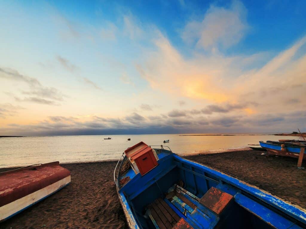 Barco azul e vermelho na praia para ilustrar o post seguro viagem Cabo Verde. - Foto: Victor Svistunov via Unsplash