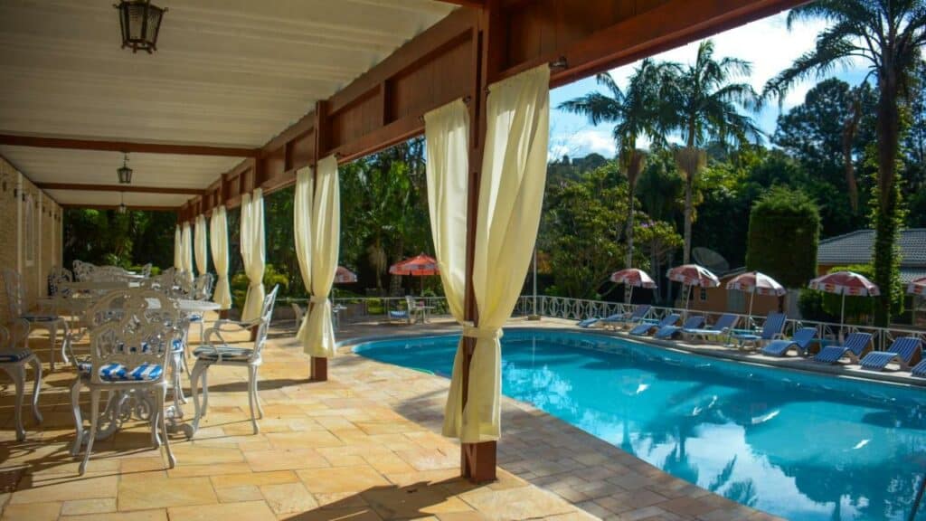 Piscina do Biazi Paradise Hotel com um deck coberto com cadeiras e o outro lado do deck é aberto com espreguiçadeiras, cercado por árvores, para representar hotéis em Serra Negra