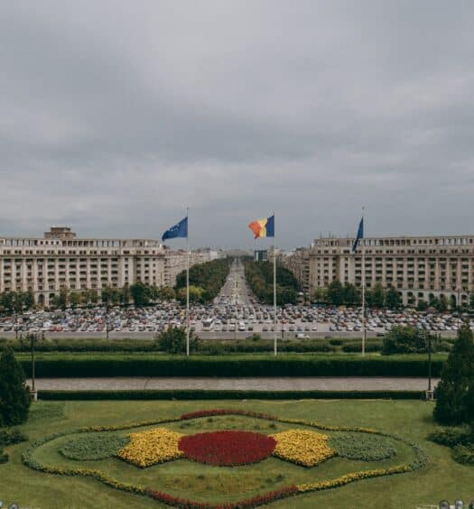 Palácio do parlamento na Romênia, construção de um palácio de época com jardim na frente e bandeiras do país.