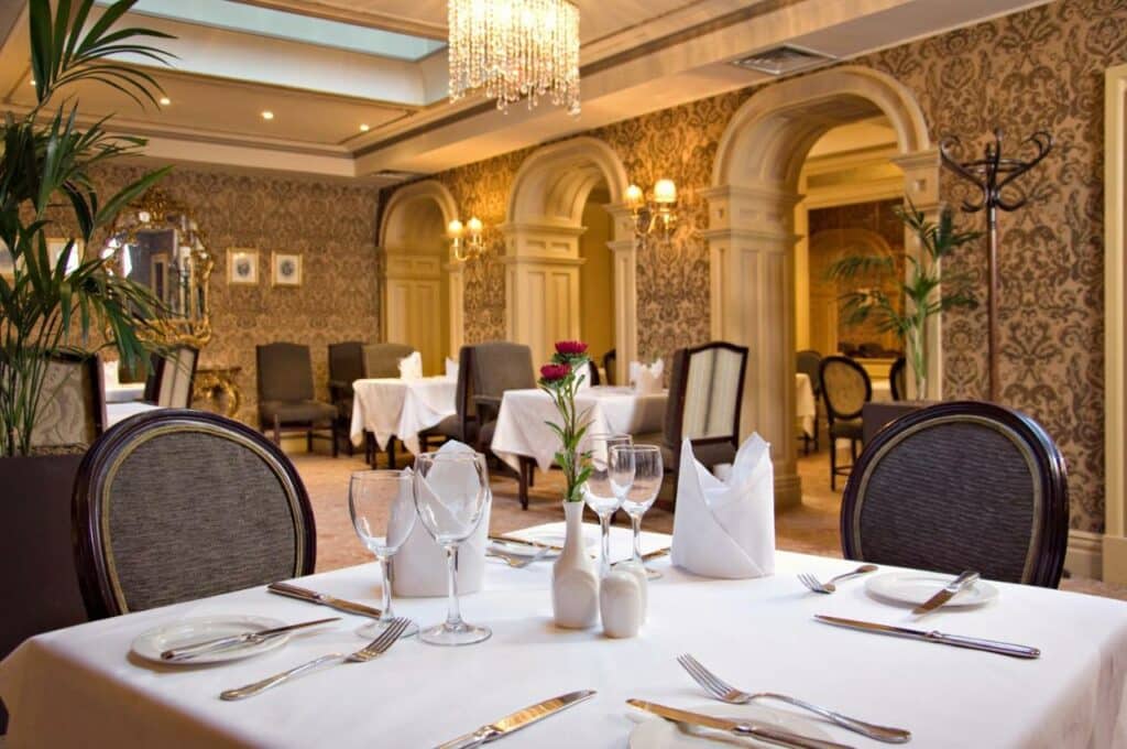 Restaurante do Buswells Hotel com um estilo vitoriano, um lustre, mesas quadradas com cadeiras estofadas