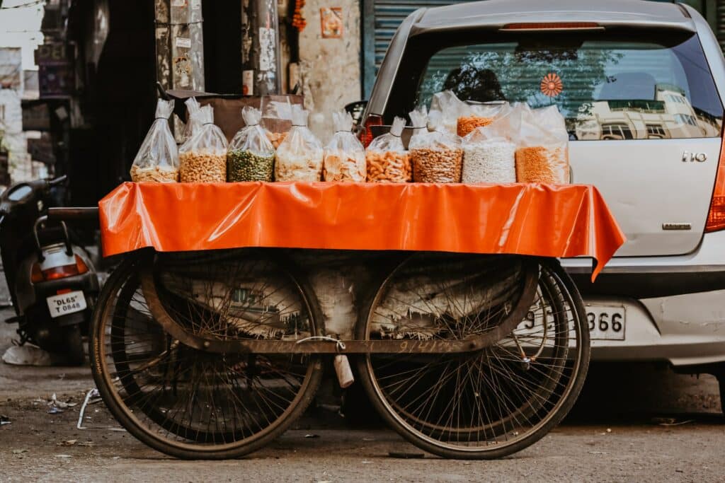 Sacos de plástico com frutas secas e sementes em cima de um tecido laranja encostado em um carro para ilustrar o post de seguro viagem Nova Deli - Foto: Ibrahim Rifath via Unsplash