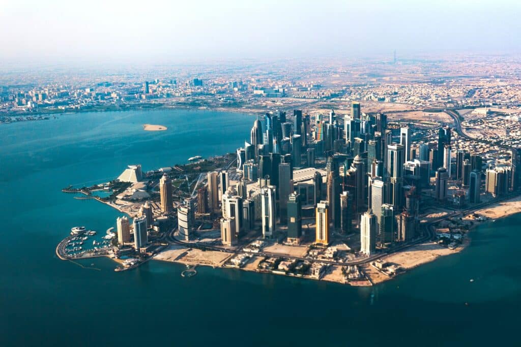 Vista aérea de Doha. Com diversos prédios altíssimos, a cidade é banhada por todo o redor pelo mar do Golfo, de águas turquesa. Representa eSIM Qatar.