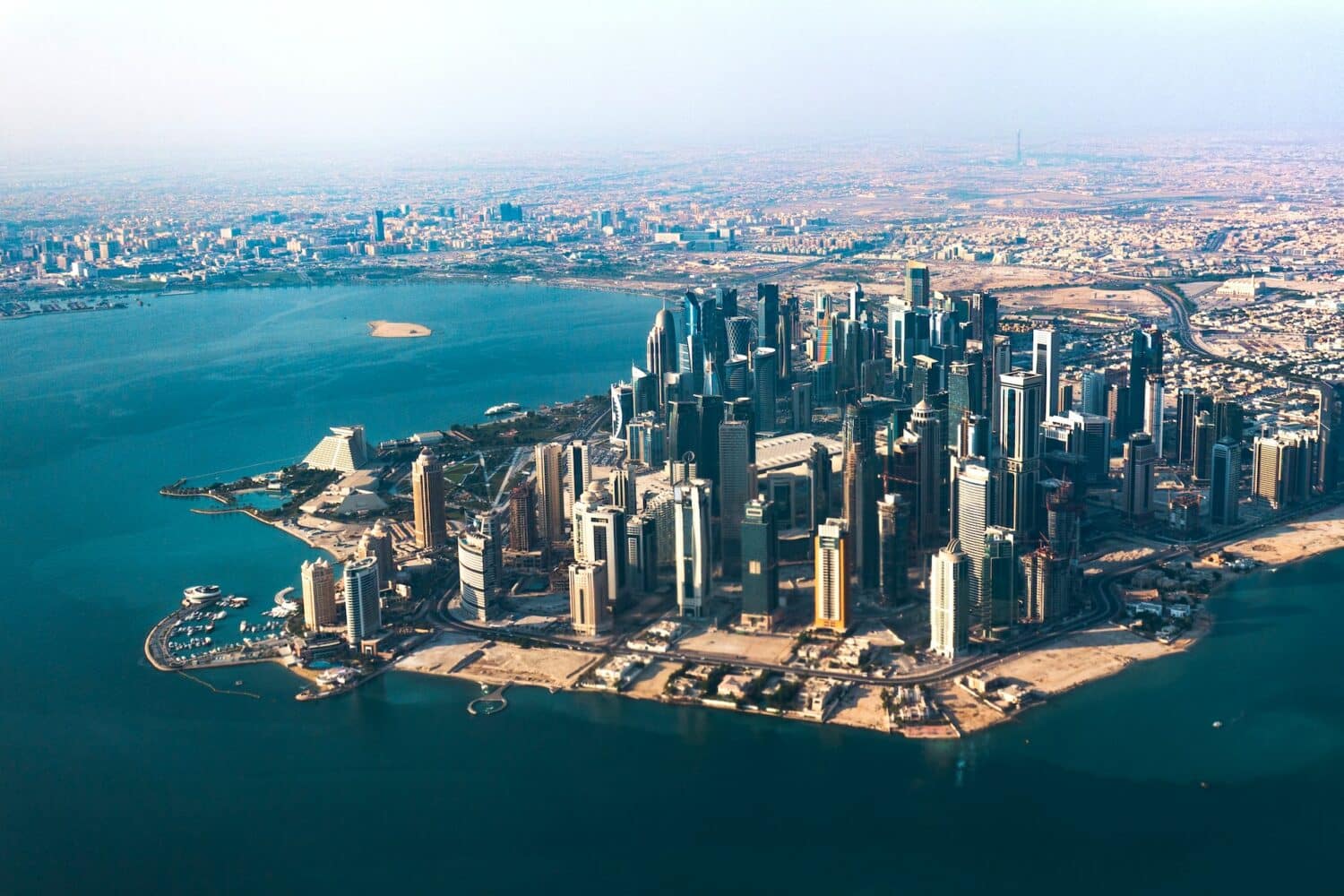 Vista aérea de Doha. Com diversos prédios altíssimos, a cidade é banhada por todo o redor pelo mar do Golfo, de águas turquesa. - Foto: Radoslaw Prekurat via Unsplash