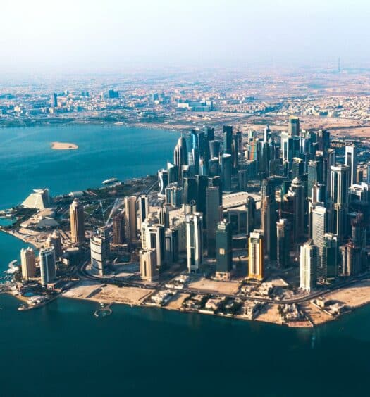Vista aérea de Doha. Com diversos prédios altíssimos, a cidade é banhada por todo o redor pelo mar do Golfo, de águas turquesa. - Foto: Radoslaw Prekurat via Unsplash