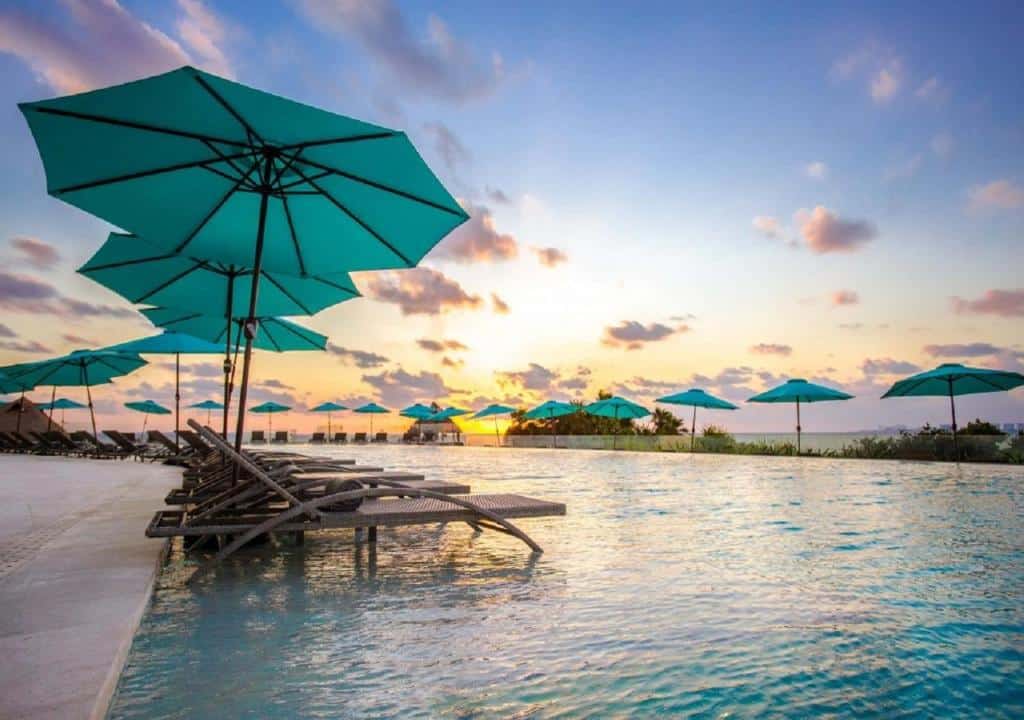 piscina ao pôr do sol no Dreams Vista Cancun Golf & Spa Resort com algumas espreguiçadeiras vazias e um céu anoitecendo em tons de azul e roxo