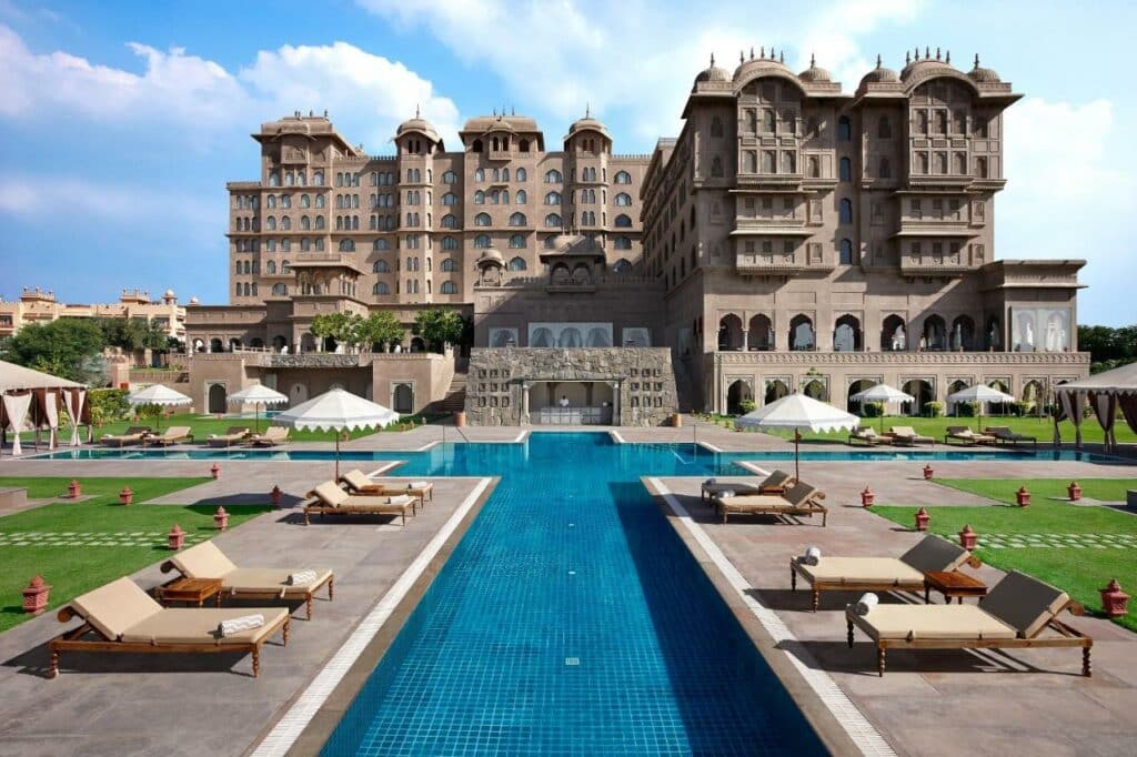 Hotel Firmont Jaipur para ilustrar o seguro viagem Jaipur. O hotel está ao fundo, com uma piscina e cadeiras de praia na frente.