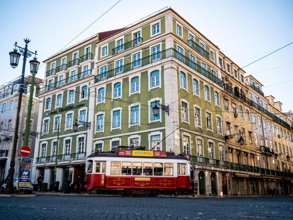 Fachada do Figueira by The Beautique Hotels, um dos hotéis em Lisboa, com paredes verdes e detalhes brancos, além de um bondinho passando em frente