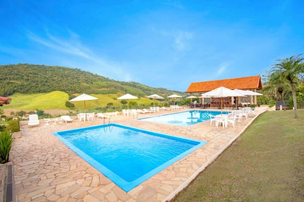 Duas piscinas do Filimahalo Hotel com muitas montanhas ao redor com um deck com mesas e cadeiras
