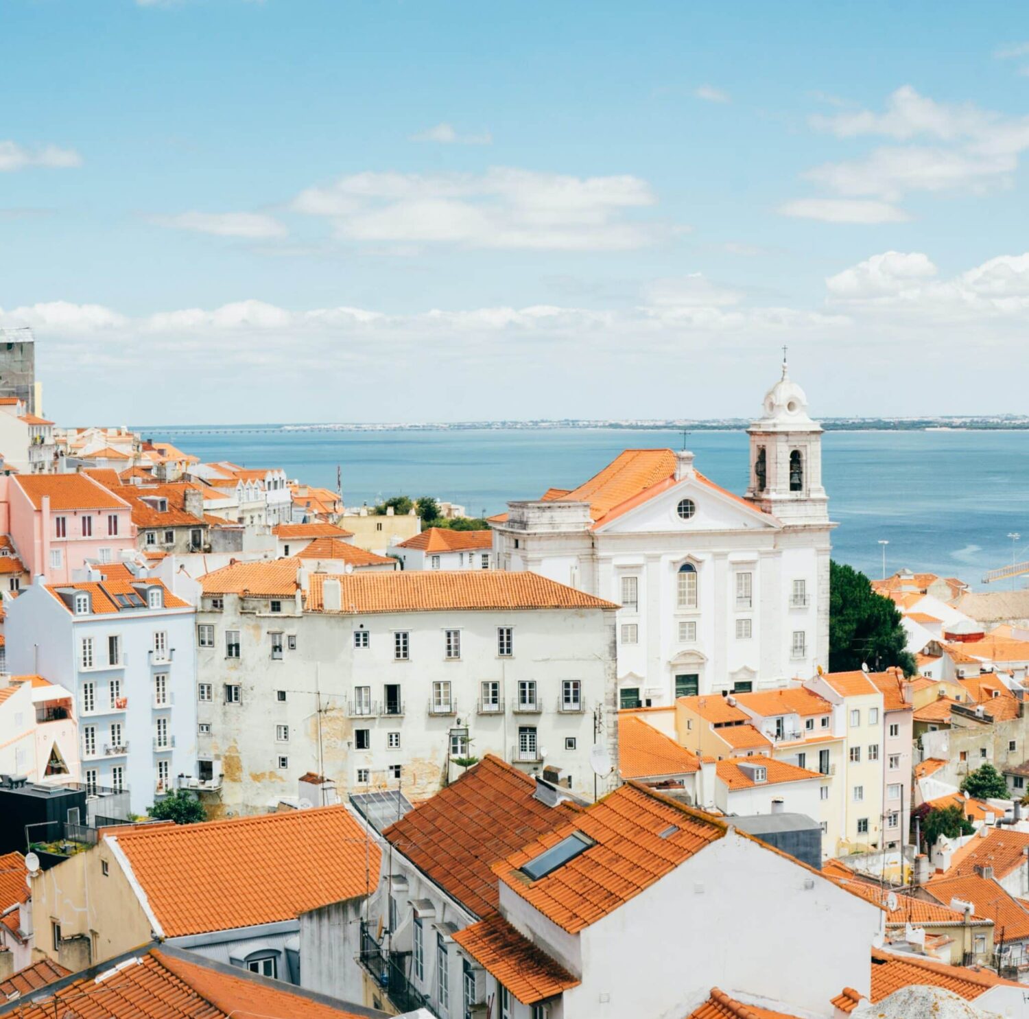 Visão sobre telhados de cor laranja, na cidade de Lisboa, e rio Tejo ao fundo, ilustrando o post sobre hotéis em Lisboa