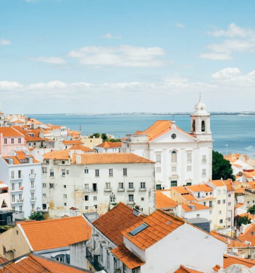 Visão sobre telhados de cor laranja, na cidade de Lisboa, e rio Tejo ao fundo, ilustrando o post sobre hotéis em Lisboa