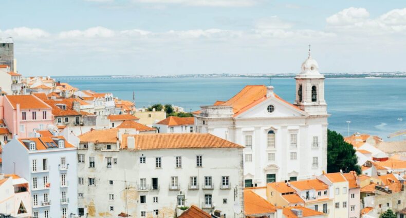 Visão sobre telhados de cor laranja, na cidade de Lisboa, e rio Tejo ao fundo, ilustrando o post sobre hotéis em Lisboa