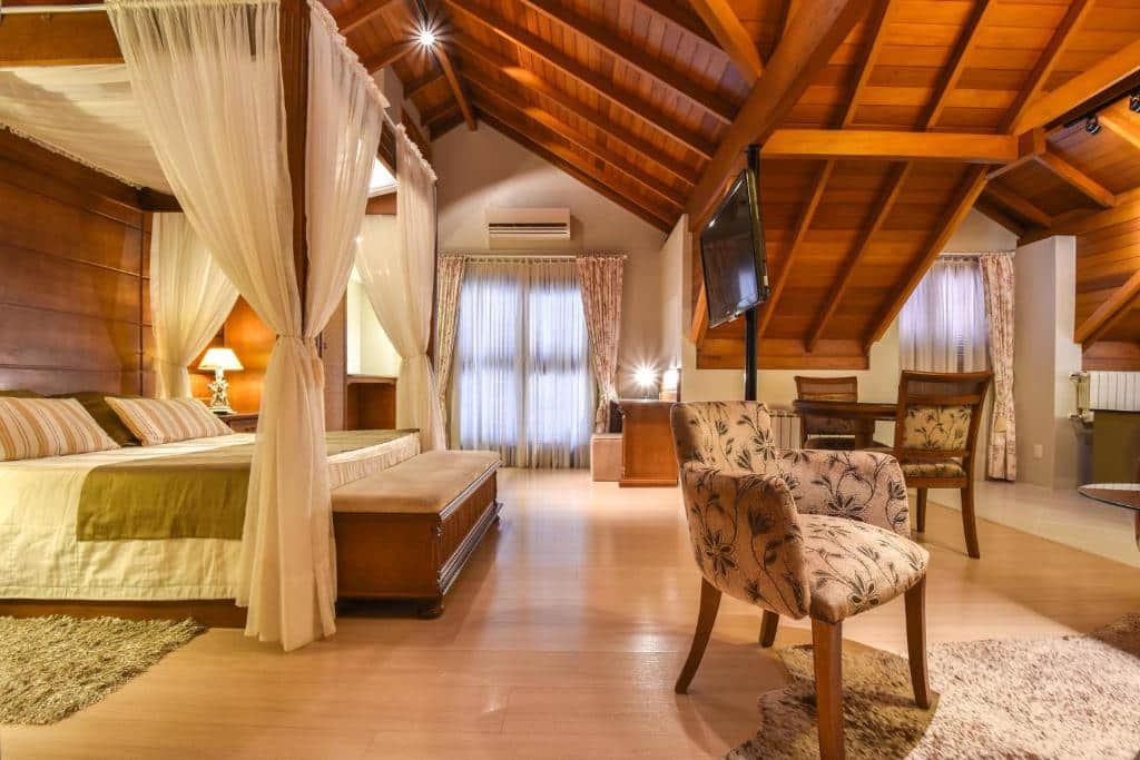 Apartamento espaçoso do Hotel Cabanas Tio Müller, com cama de casal, mesa com duas cadeiras, poltrona, TV e ar-condicionado
