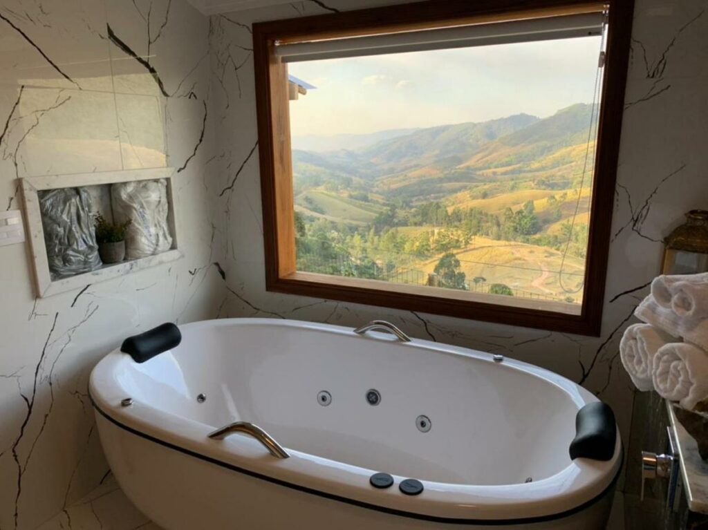 Banheira de hidromassagem com uma janela ampla dando vista para as colinas em Hotel Pousada Shangri-la, para representar hotéis em Serra Negra