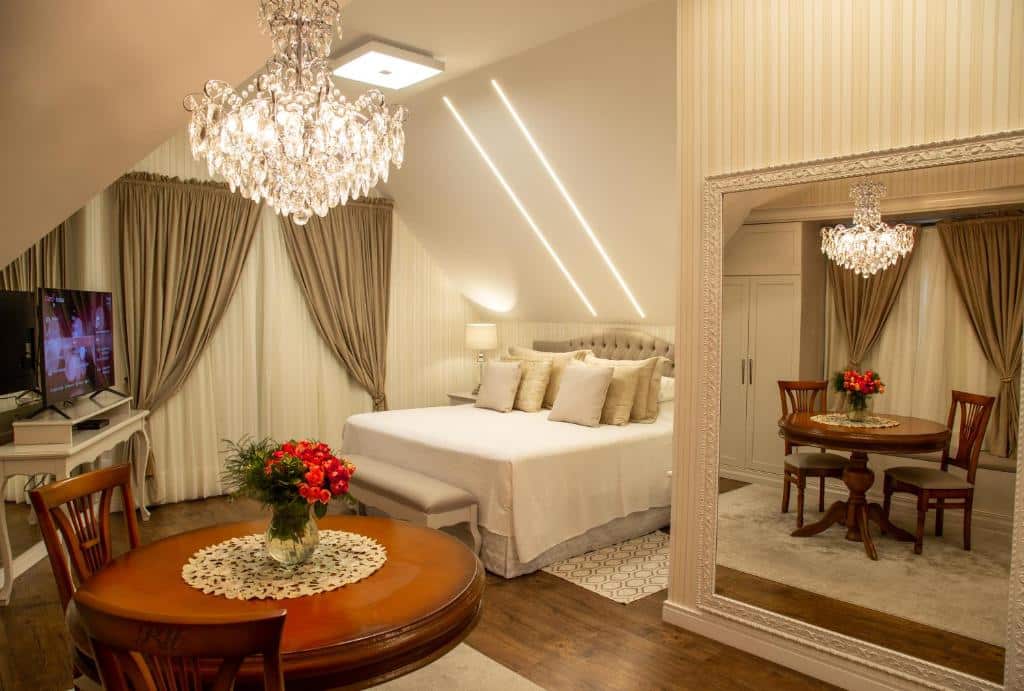 intrior do quarto do Hotel Ritta Höppner, com cama de casal, TV, espelho grande, lustre e mesa redonda de madeira com duas cadeiras