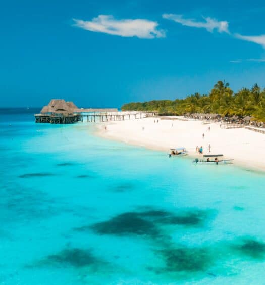Uma praia com areia branca e mar transparente com corais ao fundo do mar em Zanzibar