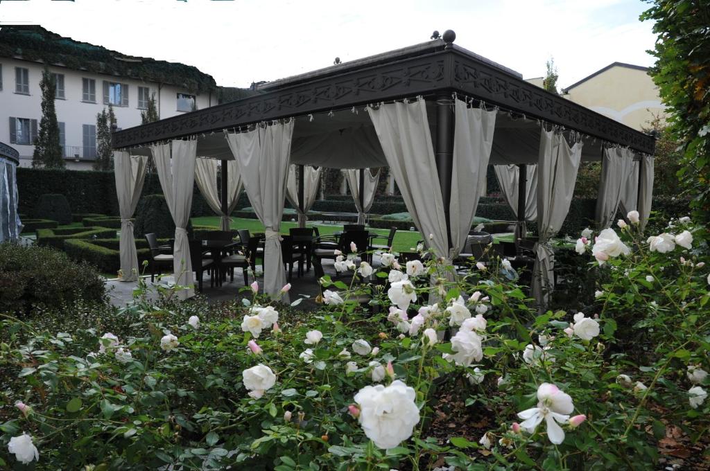 jardim com flores brancos e uma estrutura de madeira e tecido tipo uma tenda e cadeiras de madeira no Grand Visconti Palace, um dos hotéis em Milão