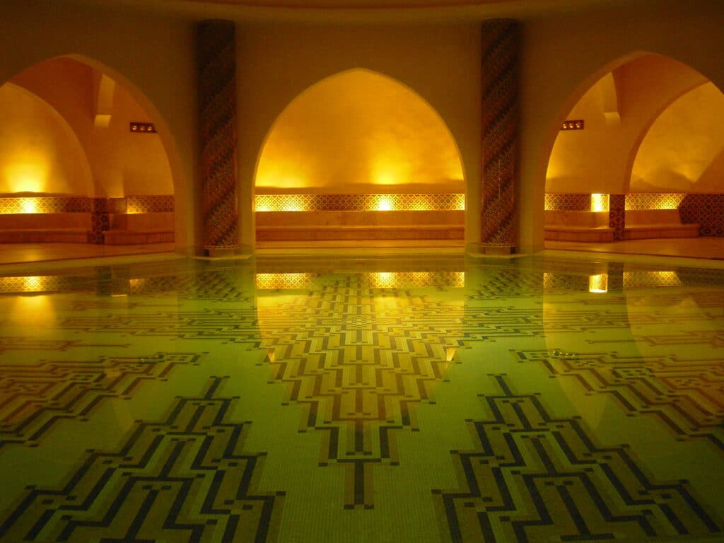 Piscina interna em um spa de Casablanca, conhecido como hammam. Ao fundo, há paredes iluminadas e arcos. - Foto: via Pxhere