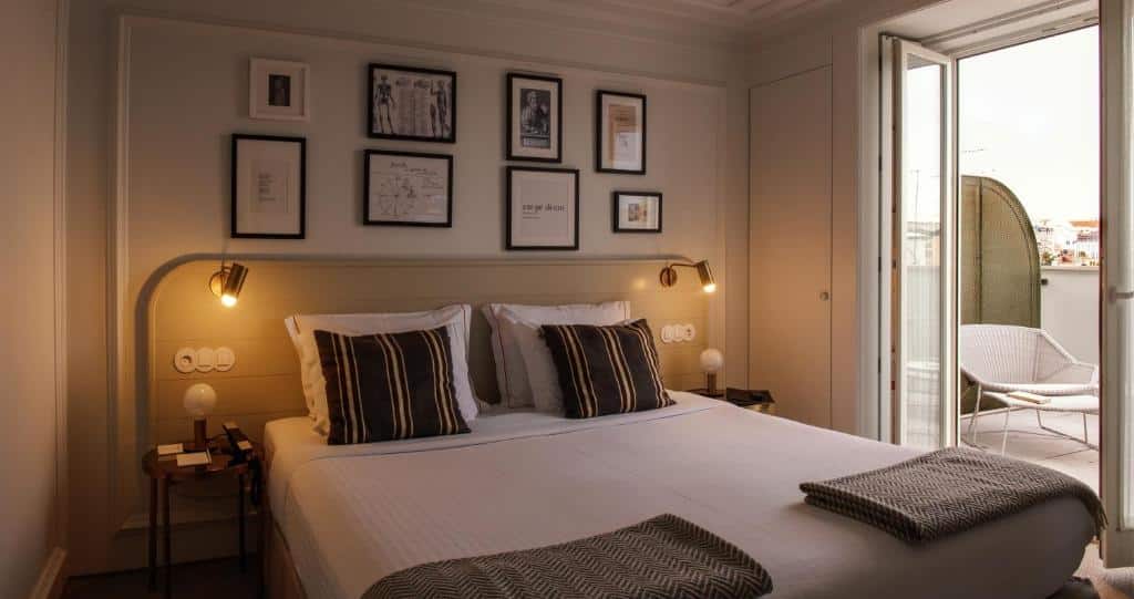 Quarto do Pessoa Lisboa Hotel, com cama de casal, luminárias acessas na cabeceira, sobre cada mesa de cabeceira, quadros na parede e sacada