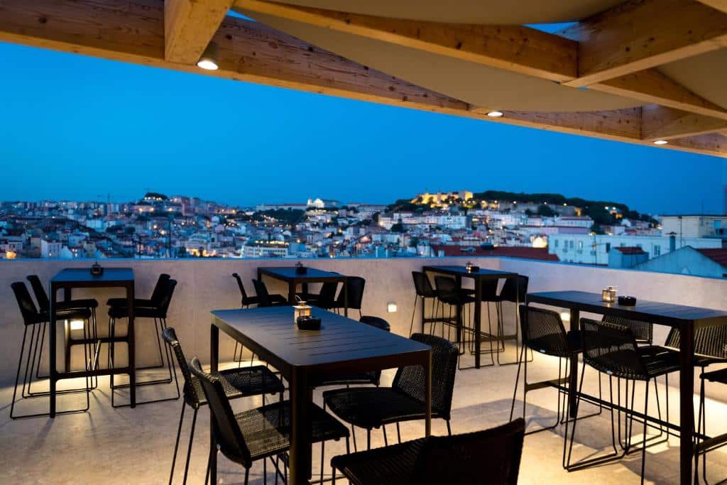 Terraço do Lisboa Pessoa Hotel com vista para a cidade, no terraço há mesas e cadeiras pretas e alguns focos de iluminação indireta, para representar hotéis no Chiado em Lisboa