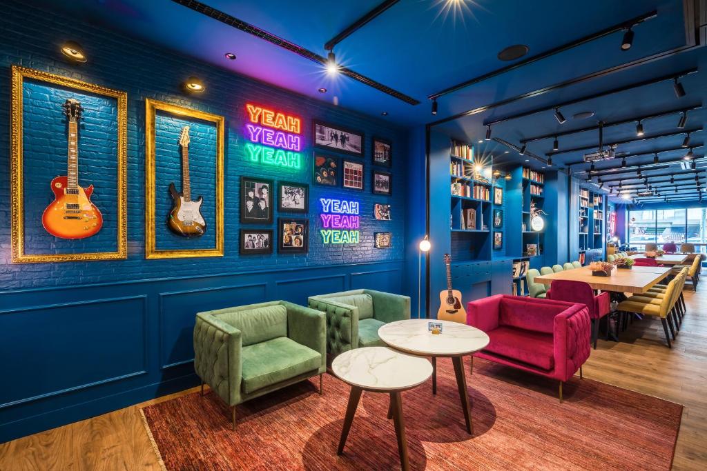 Lounge do Barceló Imagine com paredes azuis, guitarras e letreiros em neon pendurados. Sofás, mesinhas e mais decoração com motivos de música estão dispostos pelo local. Ao fundo há grandes mesas com cadeiras.