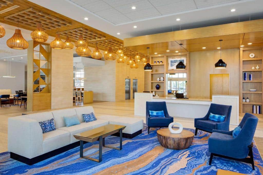lounge do Hyatt House across from Universal Orlando Resort com sofás brancos e detalhes em azul escuro, as lâmpadas e luminárias são douradas e o ambiente é bem claro e arejado