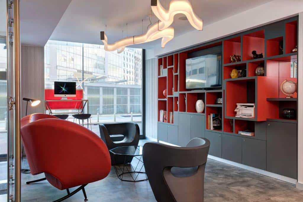 lounge com poltronas vermelhas e lâmpada com um formato diferente e sinuoso com vários nichos em tons de preto e vermelho e tv com vista da cidade no iQ Hotel Milano um dos hotéis em Milão