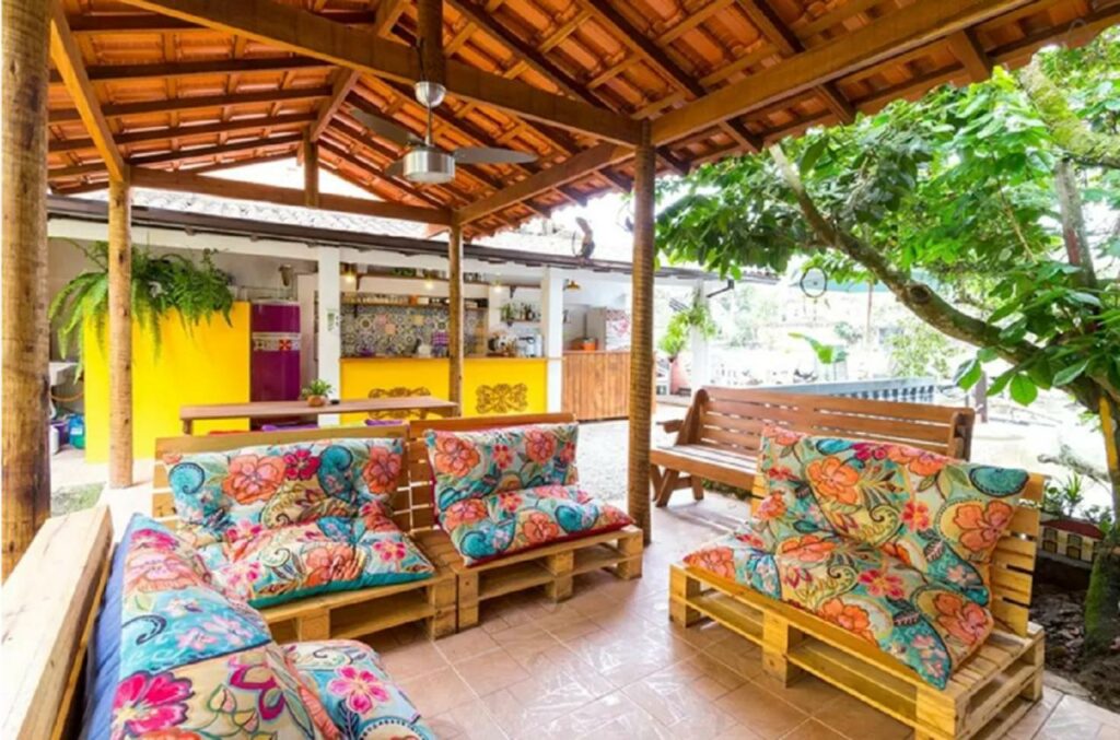 Lounge compartilhado na Maracujá Hostel com sofás floridos em uma varanda