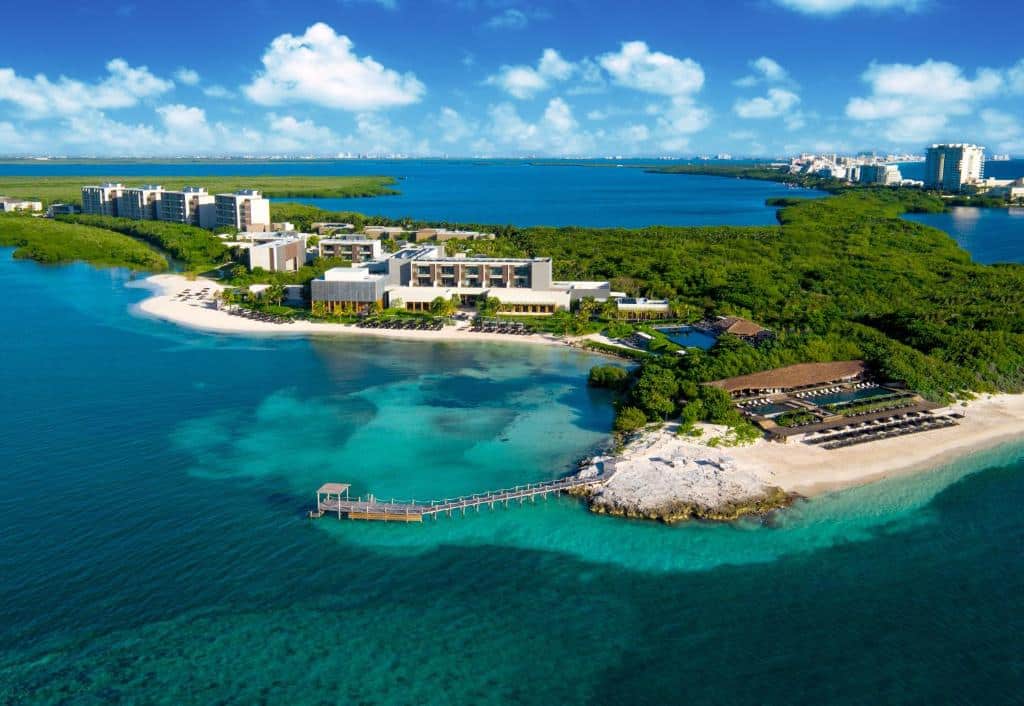 vista aérea do Nizuc Resort & Spa em Cancun com um céu azul repleto de nuvens brancas e uma península de terra com prédios e bastante vegetação verde ao redor.