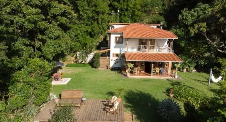 vista da pousada com dois andares e gramado com redes e mesinhas de madeira em meio à natureza, sendo uma das pousadas na Serra da Bocaina