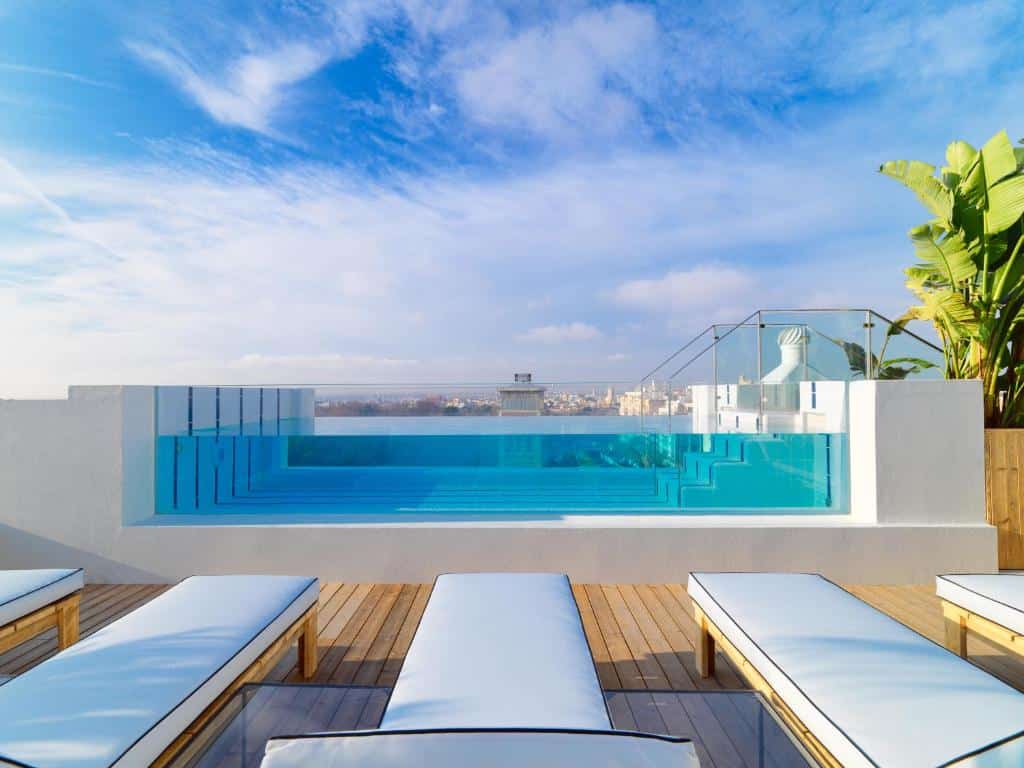 piscina com bordas de vidro em frente a espreguiçadeiras brancas no terraço com céu azul no H10 Puerta de Alcalá um dos hotéis em Madri